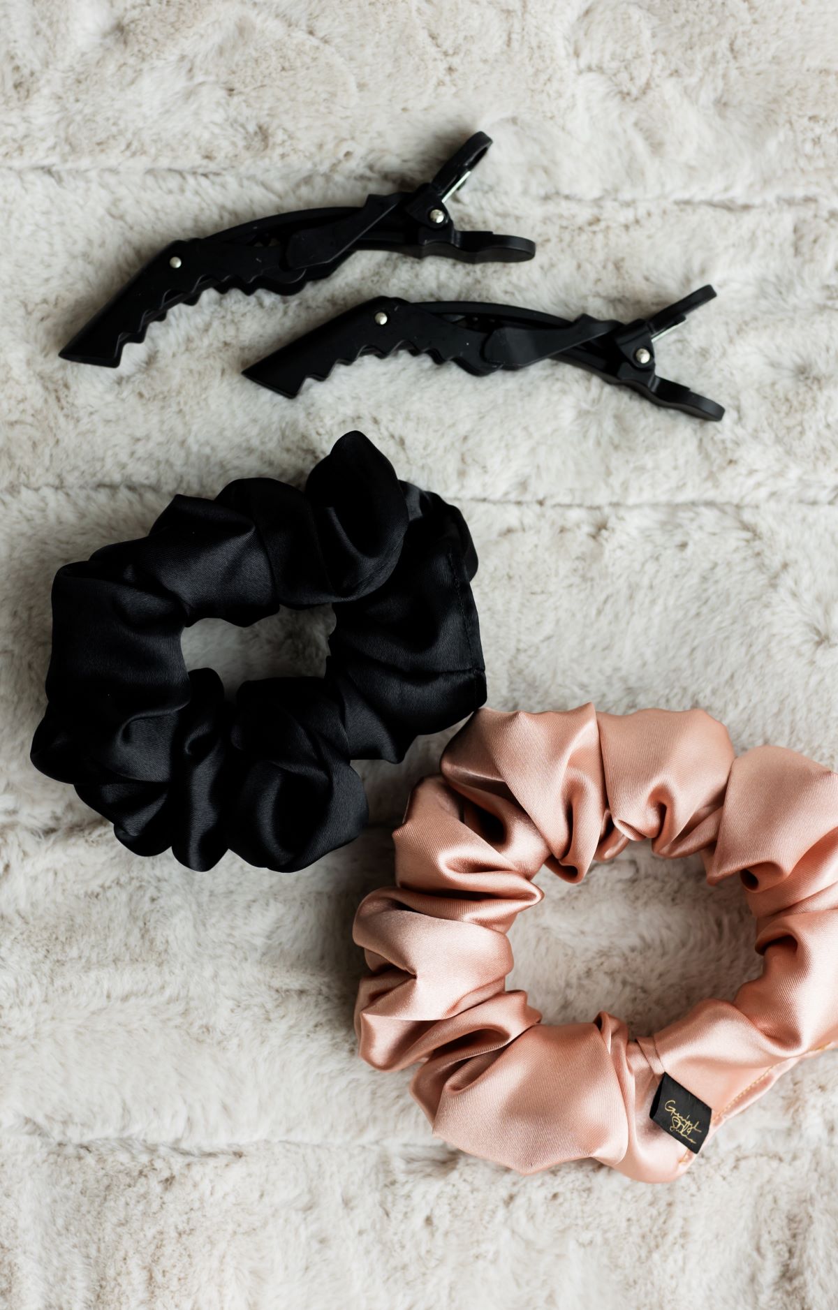 Black and blush silk scrunchies with hair clips on plush fabric in Raleigh, North Carolina.