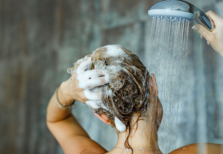 A woman washing shampoo out of her hair using a shower filter for hair extensions