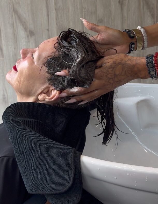 A Garnish stylist applies product to a guest's hair at the shampoo bowl