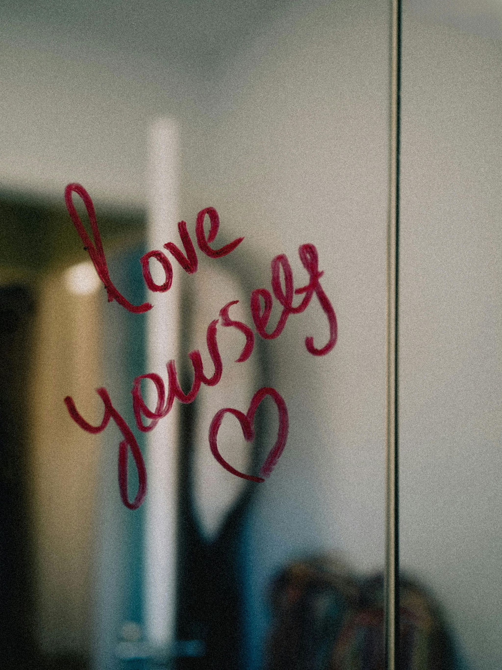 The words "love yourself" and a heart drawn on a mirror with red lipstick